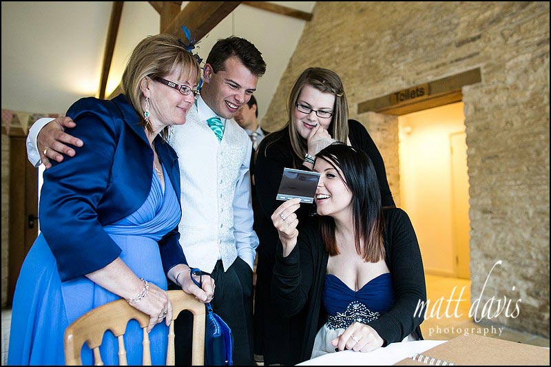 Wedding guests looking at polaroid photo taken at Kingscote Barn