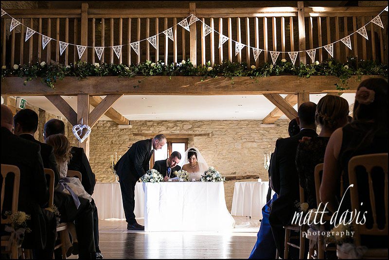 Inside Kingscote Barn signing the register during a winter wedding ceremony